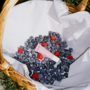 Basket of blueberries and raspberries with a pink knife on a white cloth.