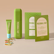 Personal Day skincare set including a green squeeze tube with a light blue cap, a tall green bottle, a green box, a green instruction card, and several small gold and pink lip balm capsules, arranged on a beige surface against a beige background.